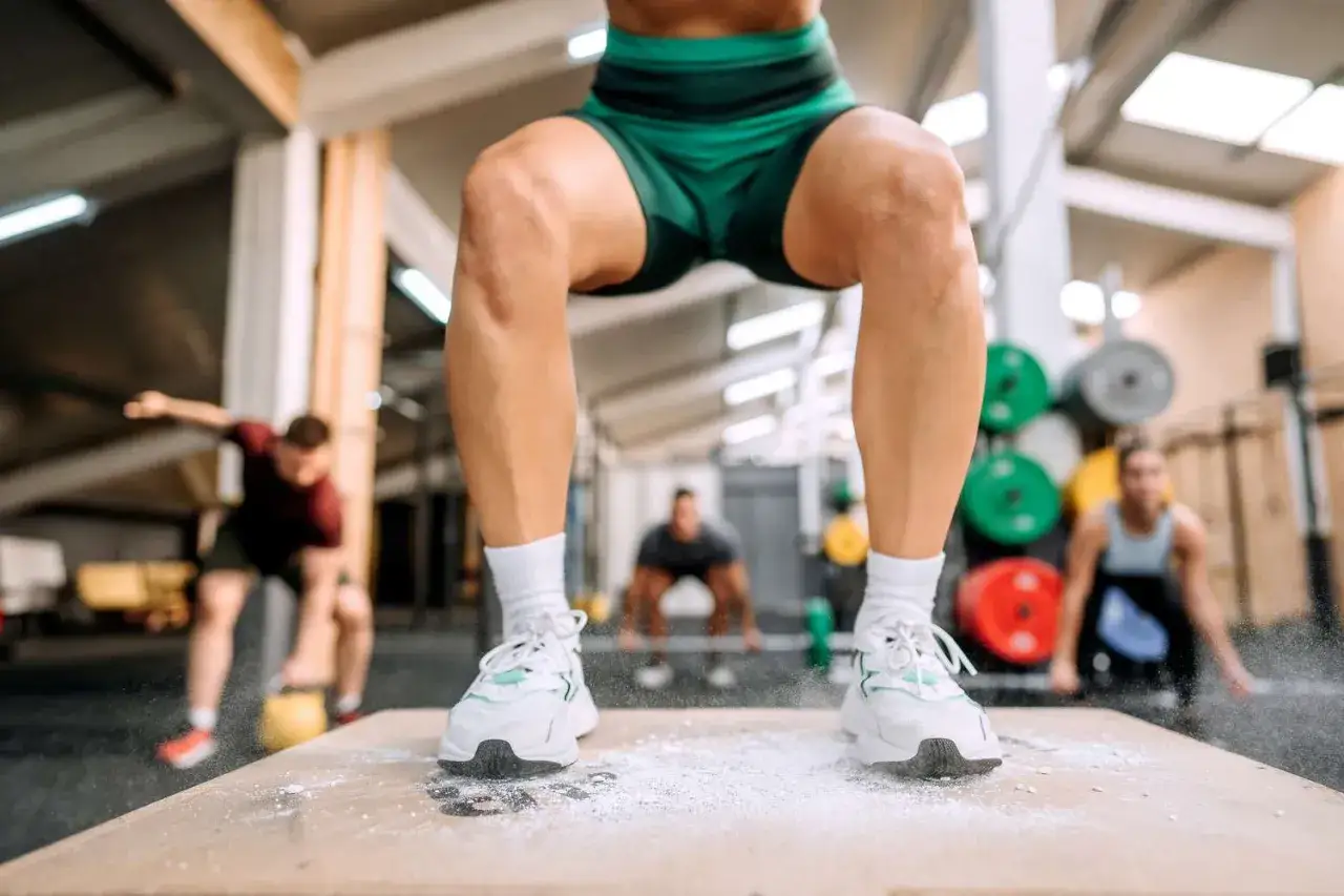 Persona haciendo sentadilla, con enfoque en la rodilla y la técnica correcta para evitar la pata de ganso. Entrenamiento para el tratamiento de la rodilla.