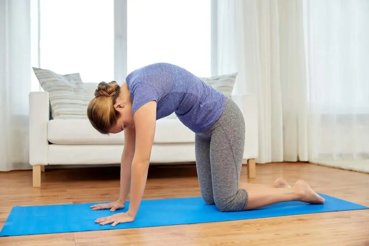 Mujer en posición de gato en una esterilla azul, ideal para ejercicios de neuralgia occipital.