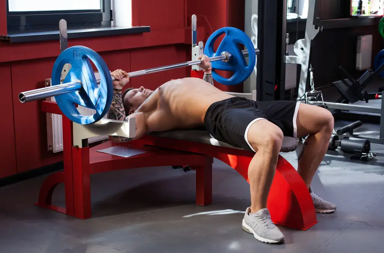 Hombre haciendo press banca con barra en un gimnasio.