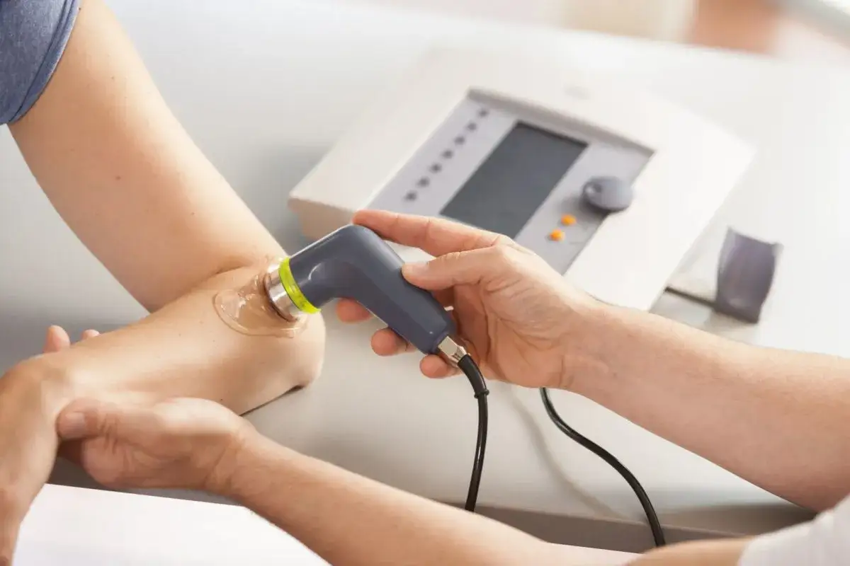 Fisioterapeuta aplica ultrasonido en el codo de un paciente con gel conductor.