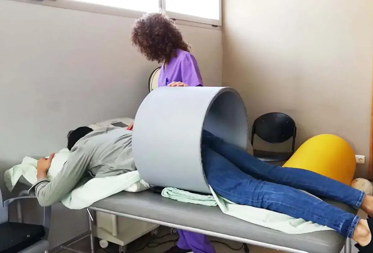 Paciente en camilla recibiendo tratamiento de magnetoterapia para artrosis, con un cilindro sobre sus piernas.