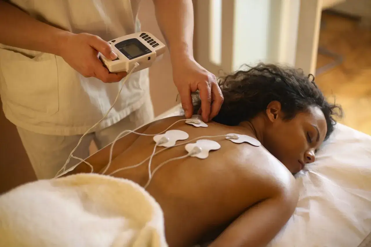 Fisioterapeuta aplica electroterapia a una paciente con parches en la espalda.