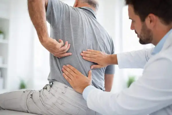 Doctor examining a patient's back, feeling for issues with the vertebras dorsales.