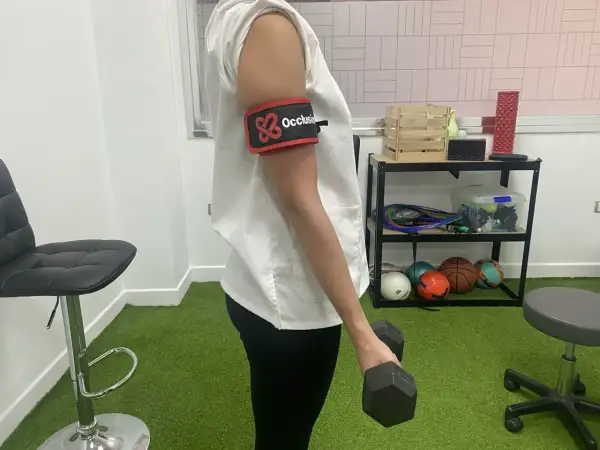 Persona con banda de oclusión en el brazo realiza ejercicios con mancuerna, parte de la rehabilitacion fractura humero ejercicios.