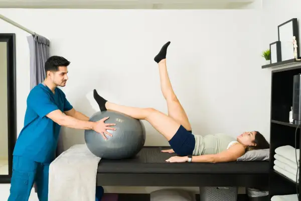 Fisioterapeuta ayuda a paciente con hiperlordosis lumbar ejercicios usando balón.