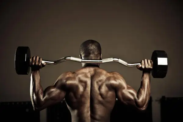 Hombre musculoso en el gym realizando ejercicios para la parte baja de la espalda con barra.