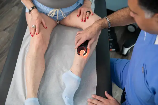 Médico examina pierna izquierda con dispositivo de luz para diagnosticar dolor.