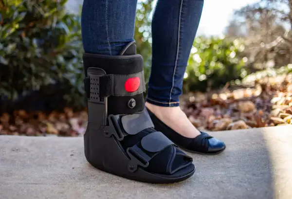 Piernas con jeans y una bota walker negra. Se puede quitar la bota walker para dormir, permitiendo usar un zapato cómodo.