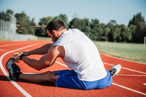 Atleta estirando en pista, cuidando sus isquiotibiales para evitar una rotura.