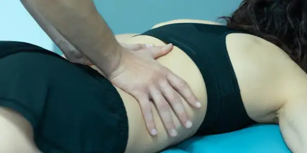 Manos de fisioterapeuta trabajando en la zona lumbar de una mujer, aliviando el crujido espalda.