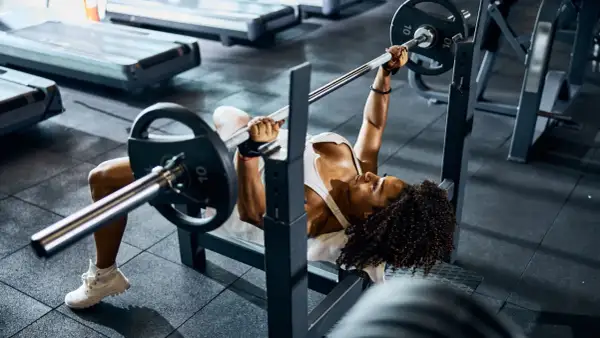 Mujer concentrada realizando press banca con barra en un gimnasio.